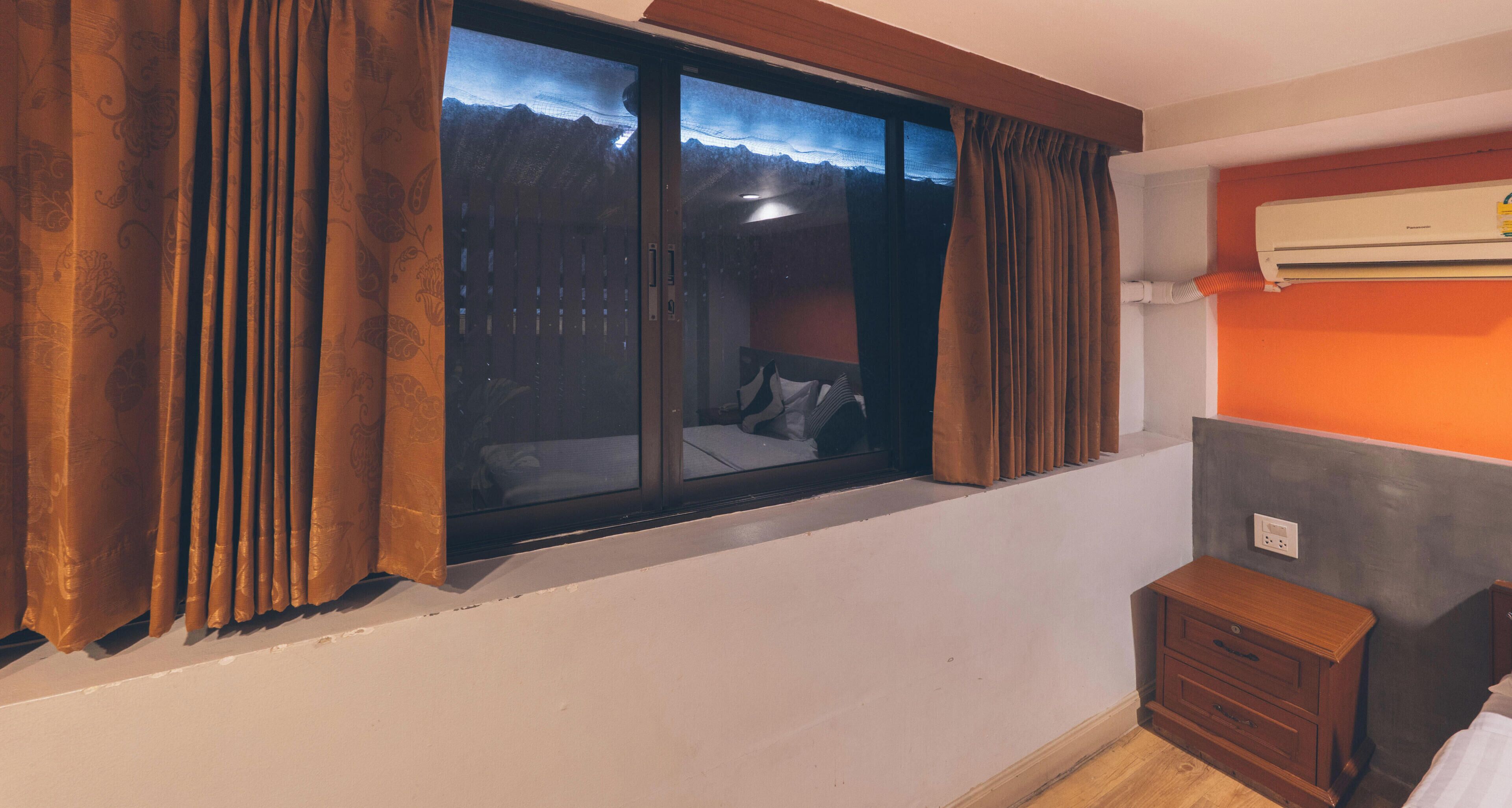 A room with a window, a bed, a nightstand, and an air conditioning unit.