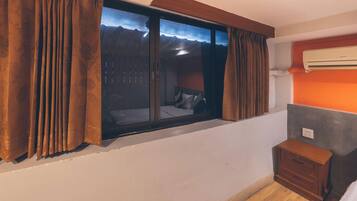 A room with a window, a bed, a nightstand, and an air conditioning unit.
