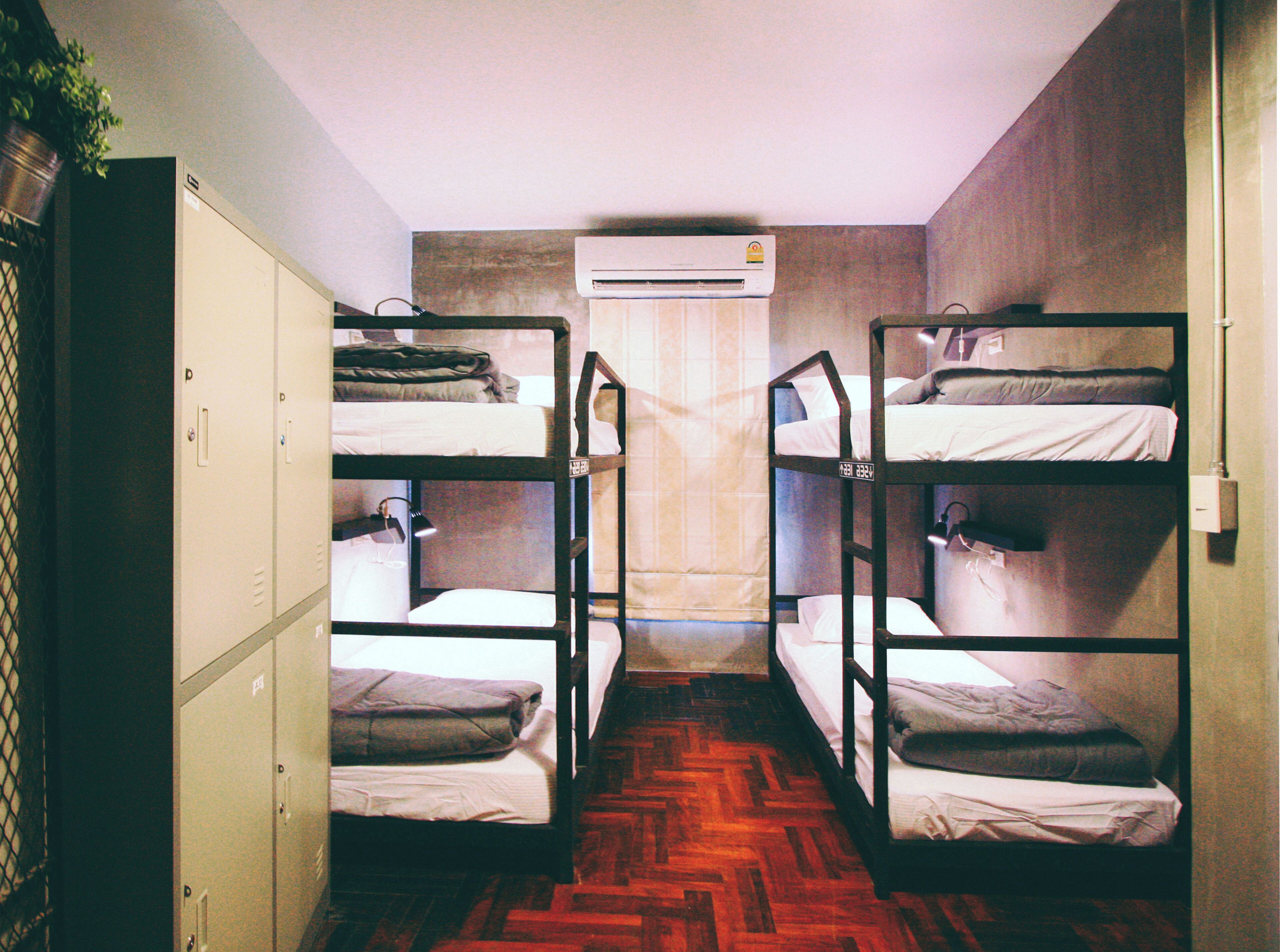 A dormitory room with bunk beds, a wardrobe, and an air conditioning unit.