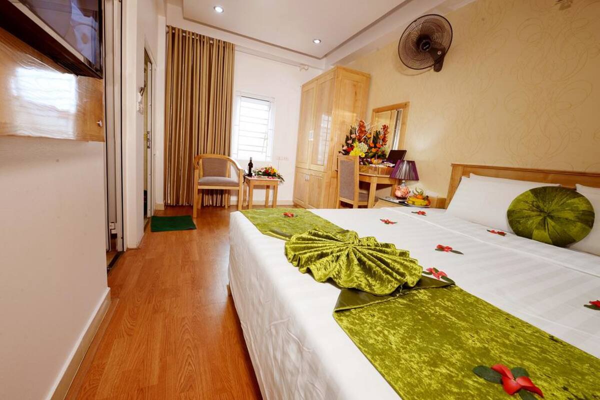 A hotel room with a bed, a chair, a desk, a mirror, and a fan.