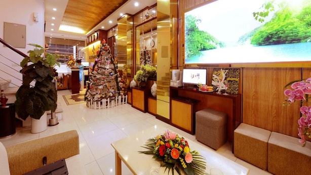 Un vestíbulo de hotel con mostrador de recepción, un árbol de Navidad y una pantalla grande mostrando un paisaje.