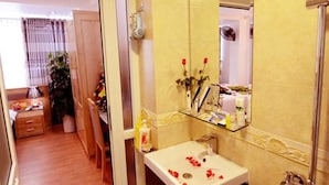 Un baño con lavamanos, espejo, ducha y una puerta que da a un comedor.