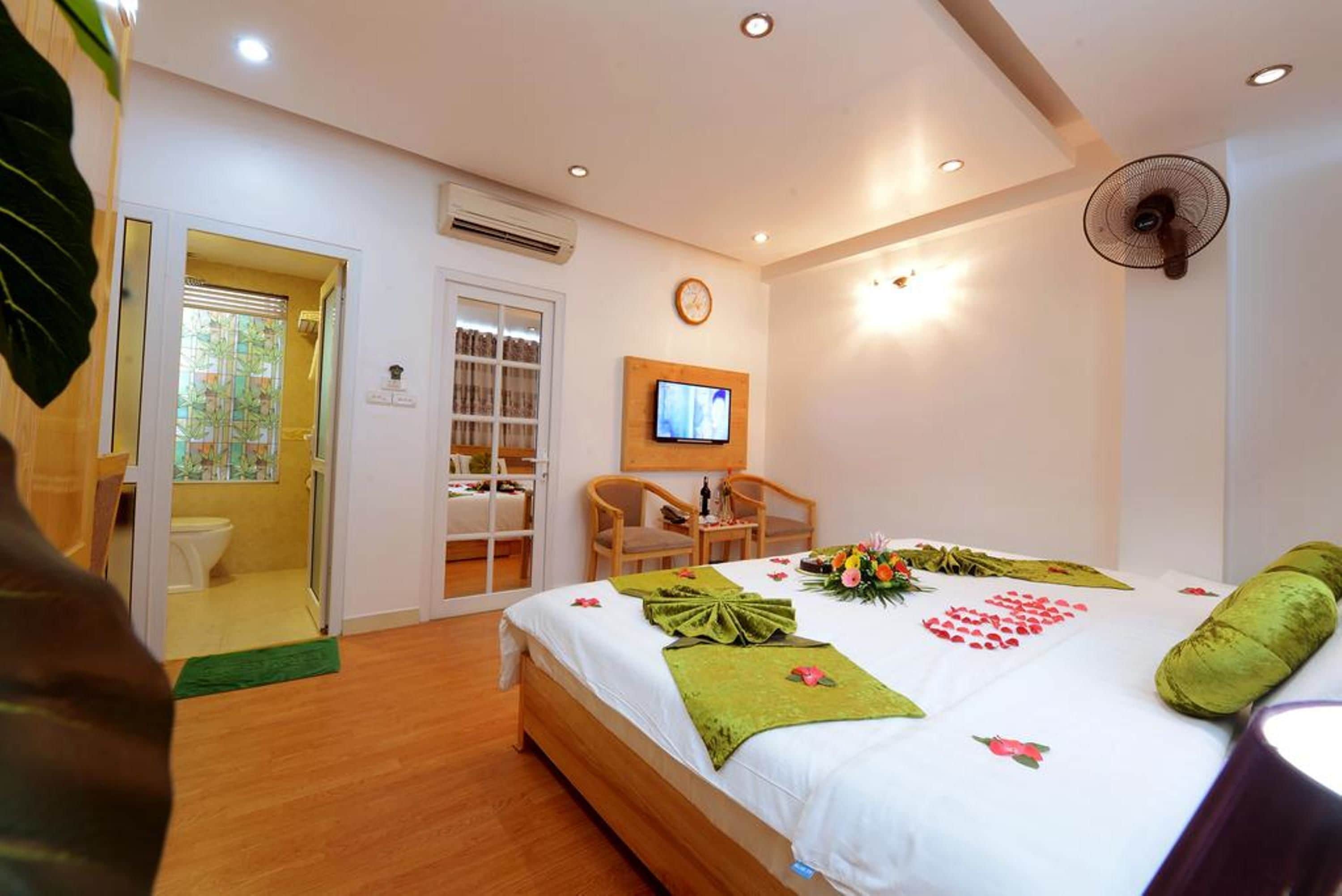 A hotel room with a bed, a television, a fan, and a bathroom with a toilet and shower.