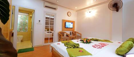 A hotel room with a bed, a television, a fan, and a bathroom with a toilet and shower.