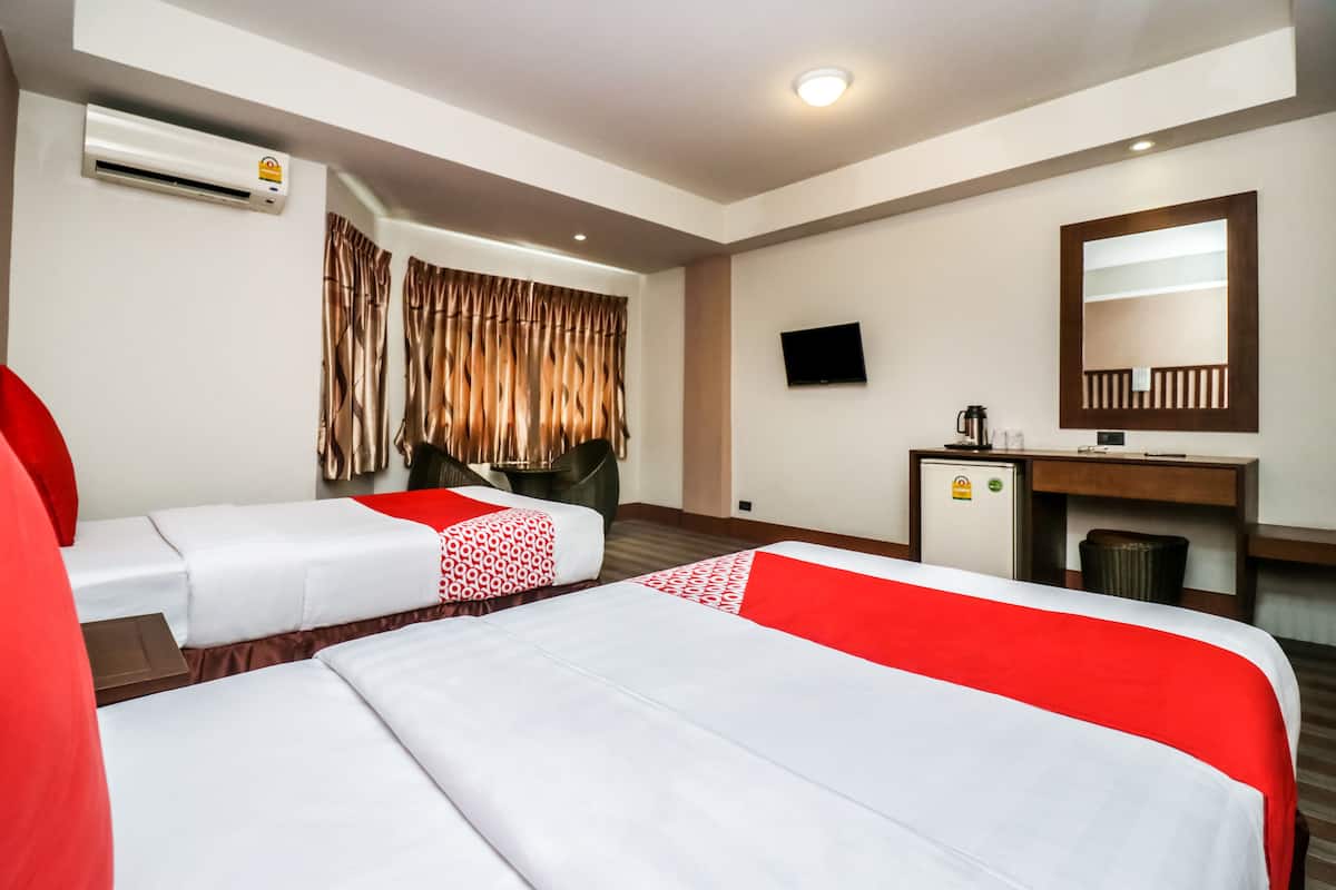 A hotel room with two beds, a desk, a TV, and an air conditioning unit.