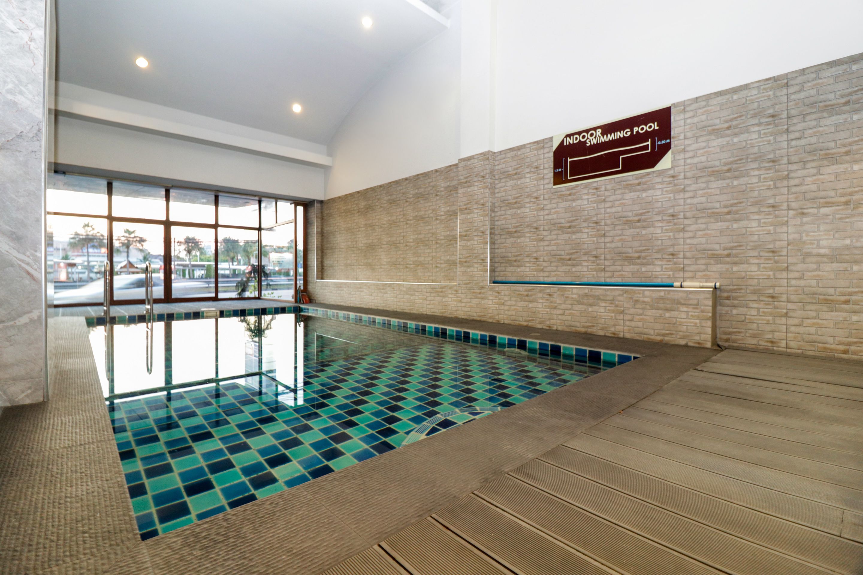An indoor swimming pool with a tiled floor, a wooden deck, and a sign indicating it is an indoor pool.