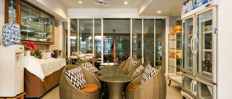 A dining area with wicker furniture, a refrigerator, and a glass display case.