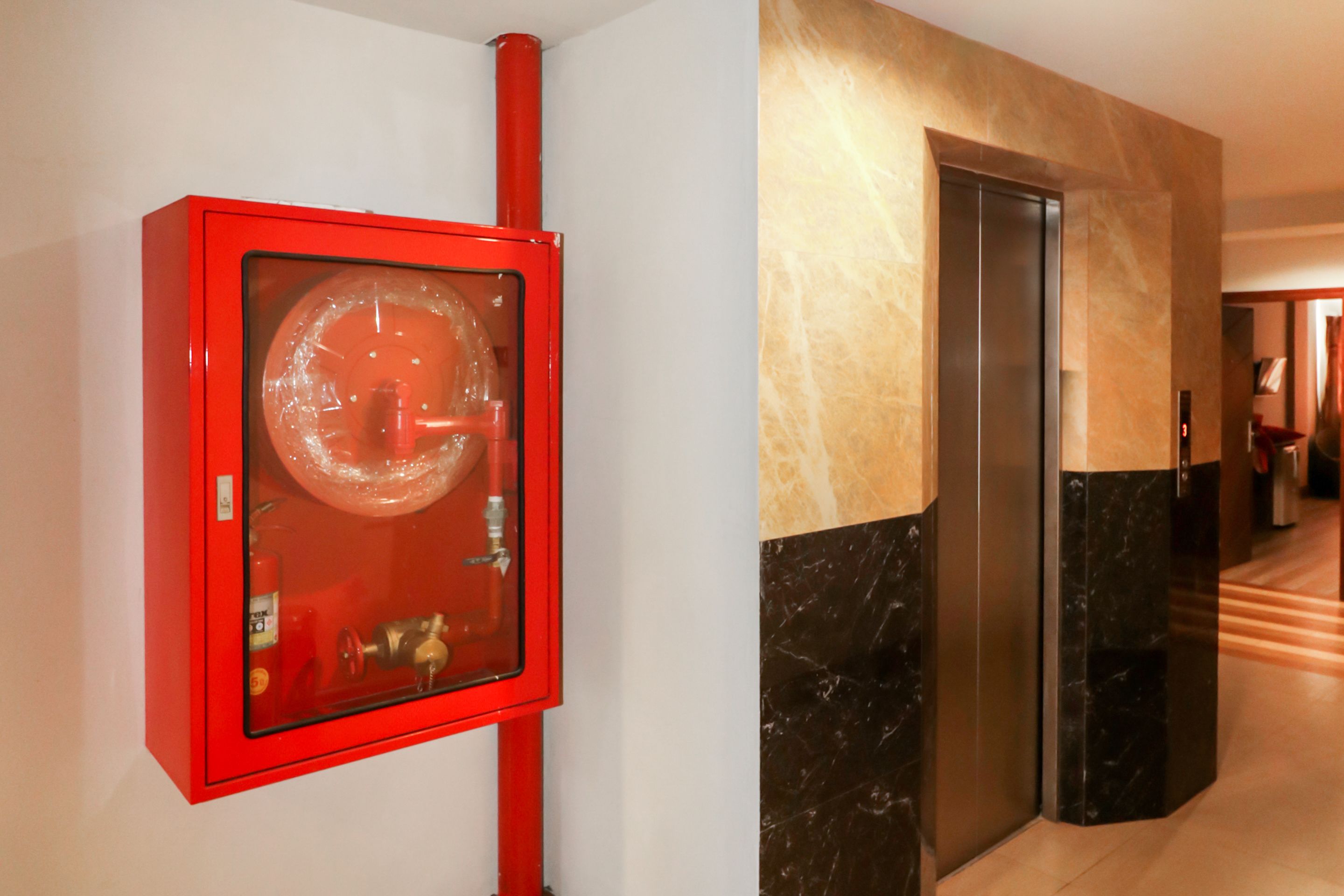 En rød brandalarmeringsboks og en moderne elevator i en gang med marmorvægge.