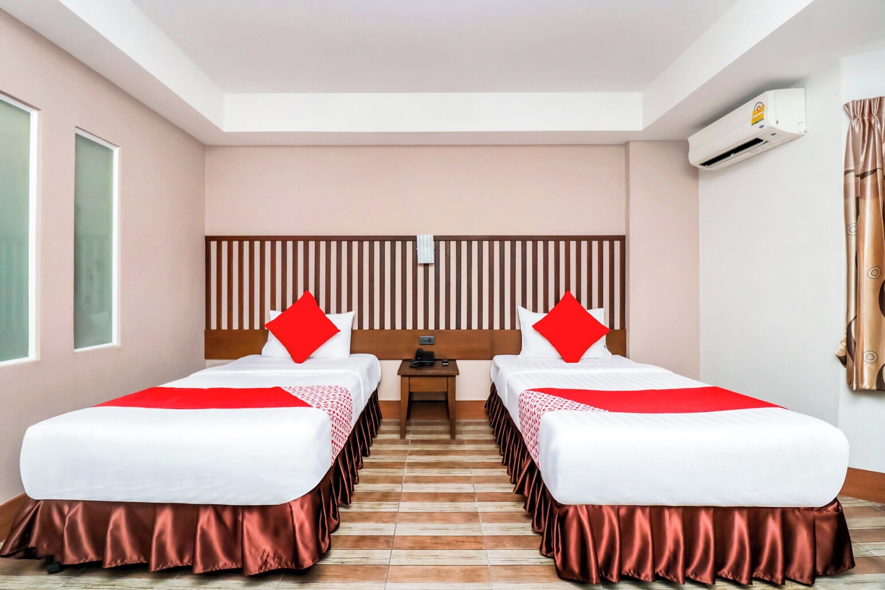 A hotel room with two beds, a headboard, a small table, and an air conditioning unit.