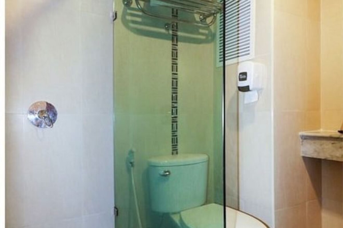 Un baño con ducha de vidrio, inodoro y lavamanos con dispensador de jabón.