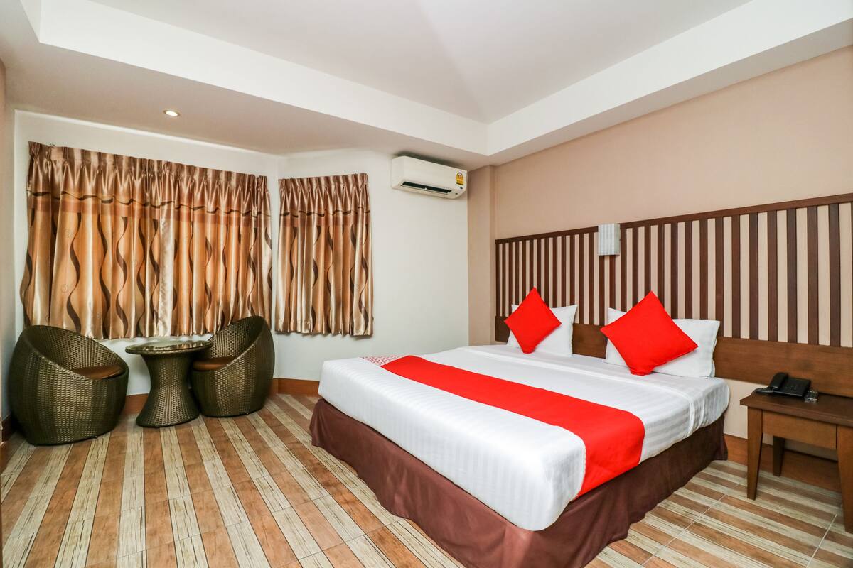 A hotel room with a large bed, two wicker chairs, a small table, and a wooden nightstand.