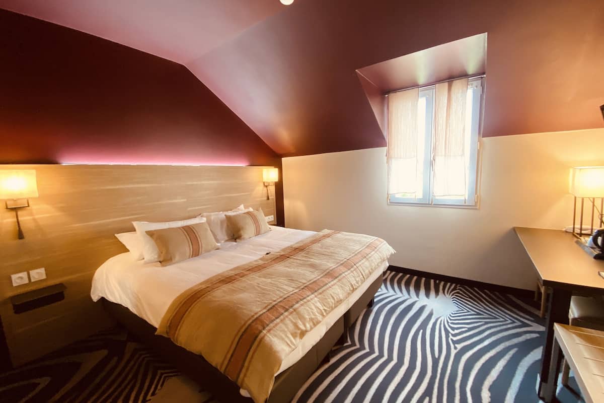 A bedroom with a bed, a window, a desk, and a zebra-patterned rug.