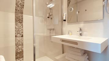 A modern bathroom with a glass-enclosed shower, a white sink, and a large mirror.