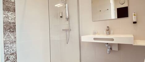Un baño moderno con ducha de vidrio, lavamanos blanco y un espejo grande.
