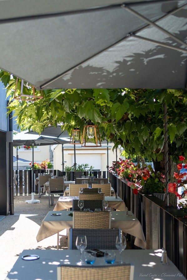 An outdoor dining area with tables and chairs, covered by a canopy, and surrounded by greenery and flowers. - Le Relais des Gourmands (Gramat)