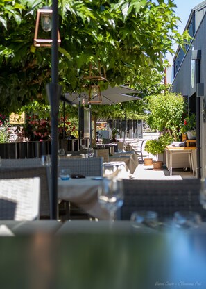 An outdoor dining area with tables and chairs, surrounded by greenery and a building in the background. - Le Relais des Gourmands (Gramat)
