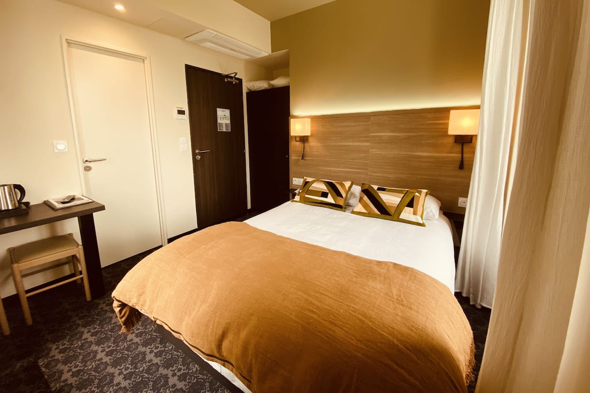 A hotel room with a bed, a desk, a chair, and a door.