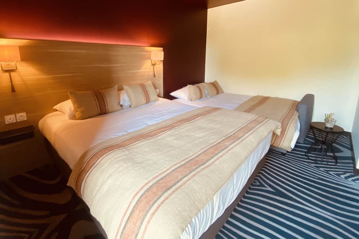 A hotel room with a large bed, a bedside table, a lamp, and a small table with a vase.