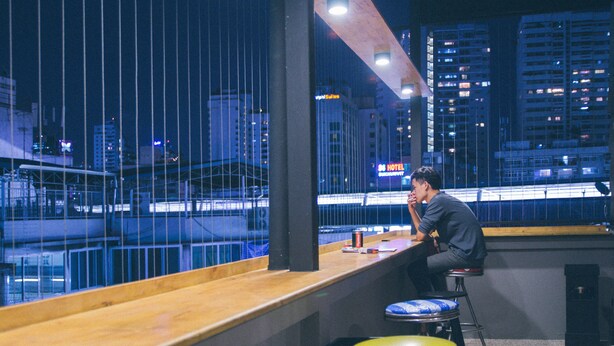 A man sitting at a bar with a view of a cityscape at night.