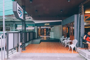 A hotel entrance with a tiled patio, outdoor seating, and a visible sign for 'Atlas'. - A7 Hidden Hostel (Bangkok)