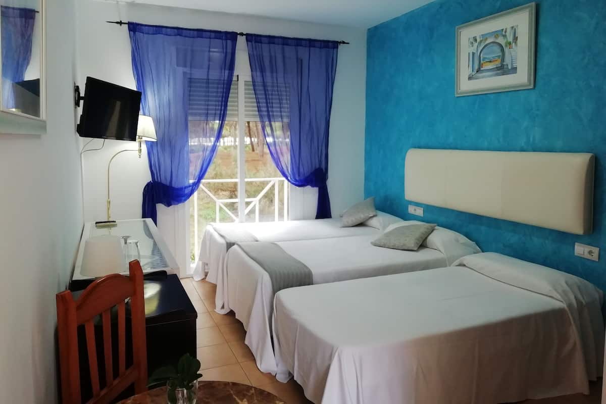 A hotel room with two beds, a desk, a chair, a TV, and a window with blue curtains.