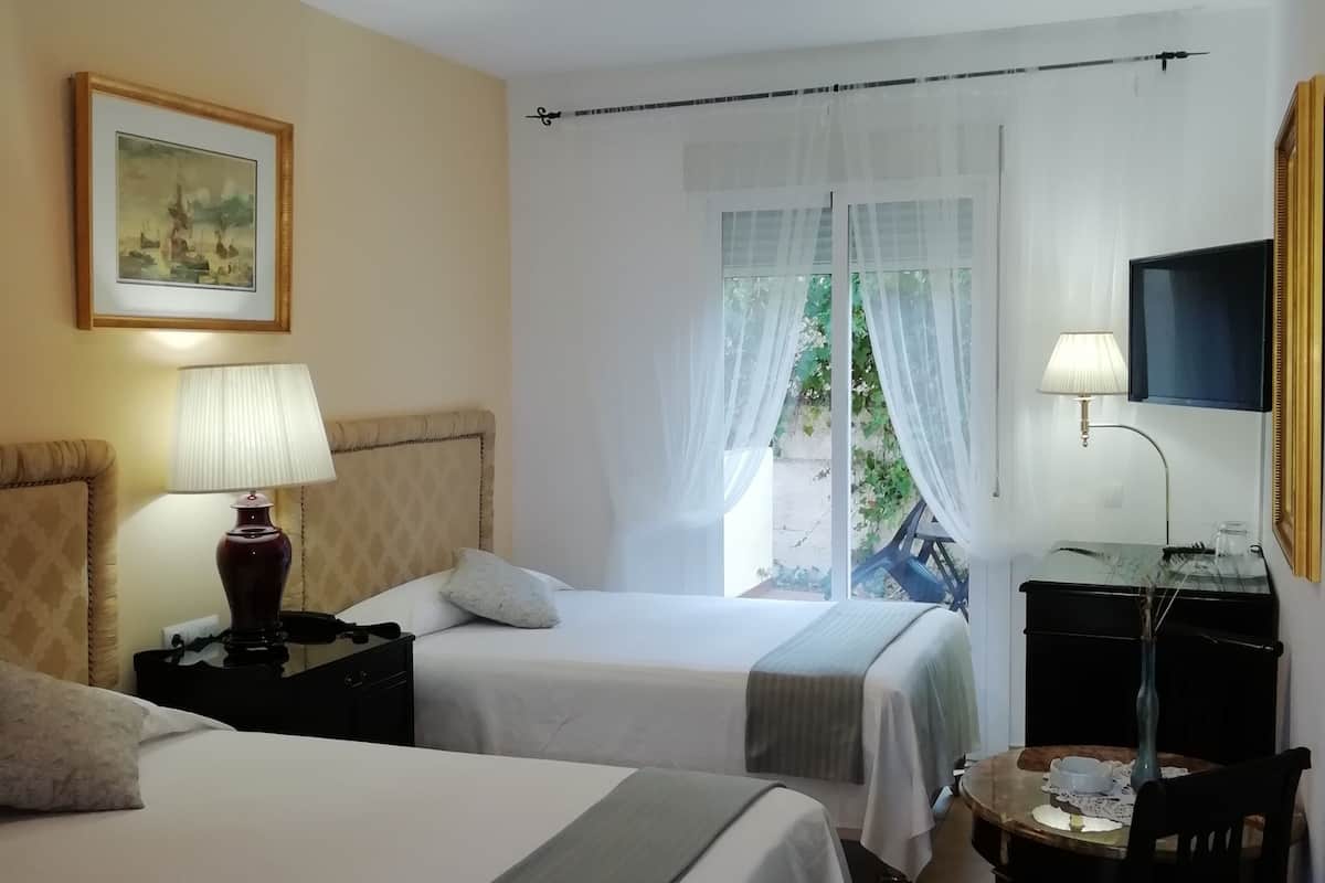 A hotel room with two beds, a desk with a chair, a TV, and a window with sheer curtains.
