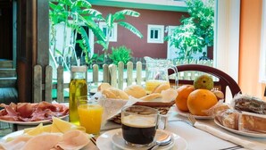 A breakfast table with plates of ham, cheese, bread, and fruit, along with a pitcher of orange juice and a glass of coffee. - Hostal Alhaja Playa (El Puerto de Santa Maria)