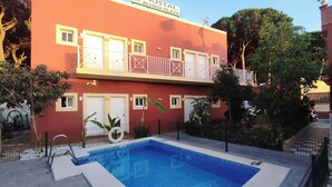 A hotel with a pool, a red facade, and balconies with white railings. - Hostal Alhaja Playa (El Puerto de Santa Maria)