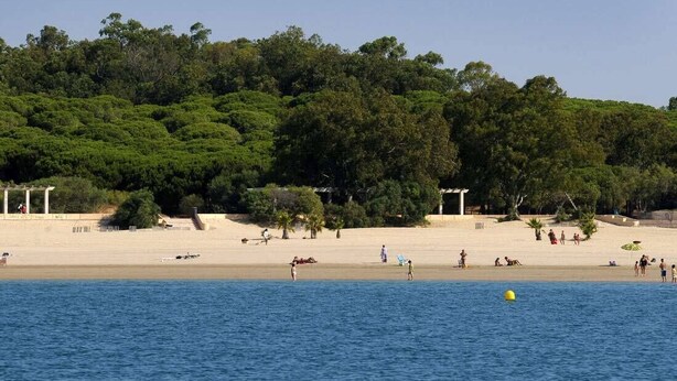 A beach with people, a sandy shore, and a forested hill in the background. - Hostal Alhaja Playa (El Puerto de Santa Maria)