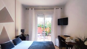 A hotel room with a bed, a desk, a TV, and a view of the outdoors. - Hostal Alhaja Playa (El Puerto de Santa Maria)