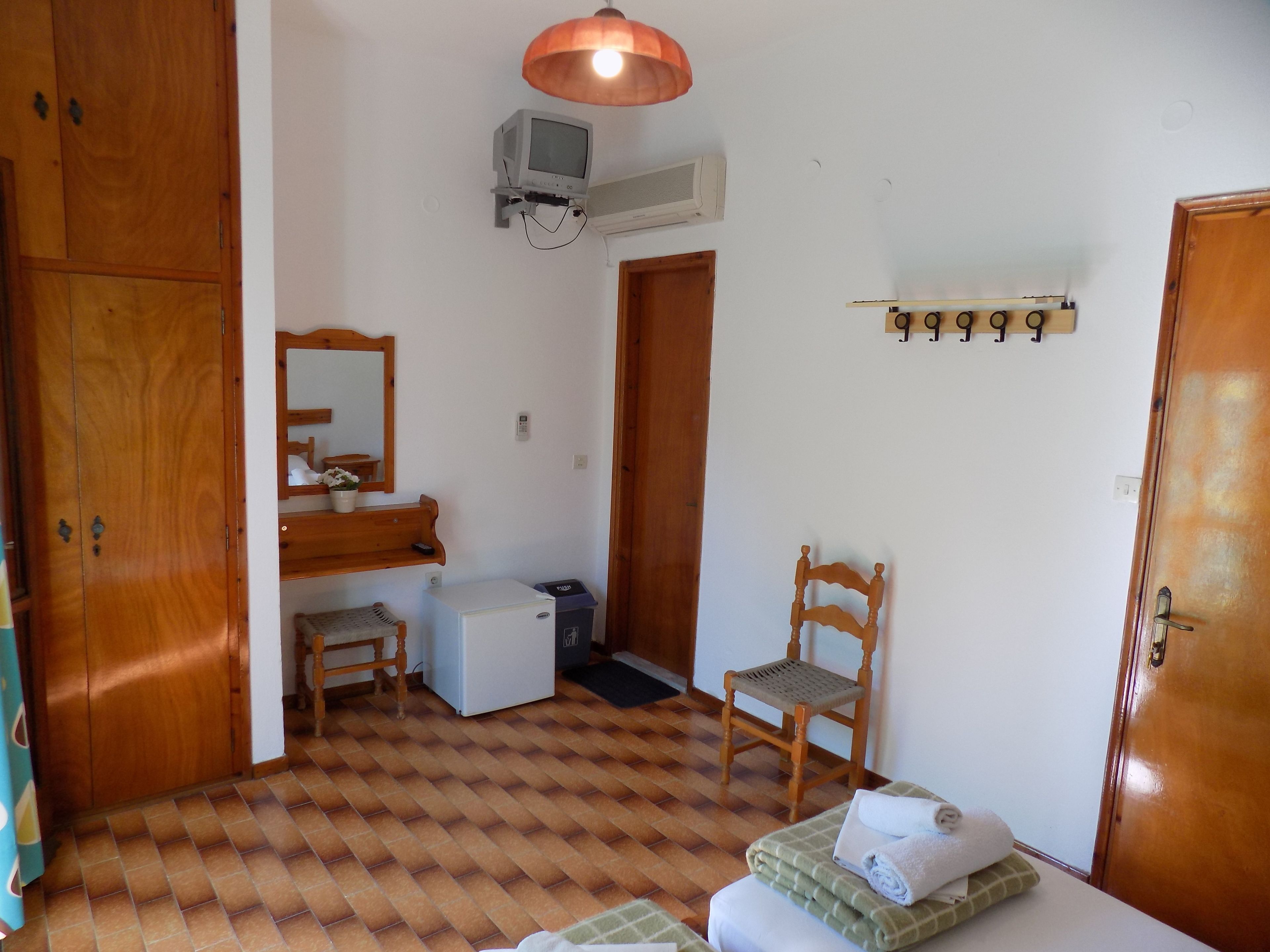 Una habitación pequeña y limpia con un armario de madera, un escritorio pequeño, una silla, una cama con una manta verde a cuadros y un calentador de pared.