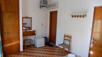 Una habitación pequeña y limpia con un armario de madera, un escritorio pequeño, una silla, una cama con una manta verde a cuadros y un calentador de pared.