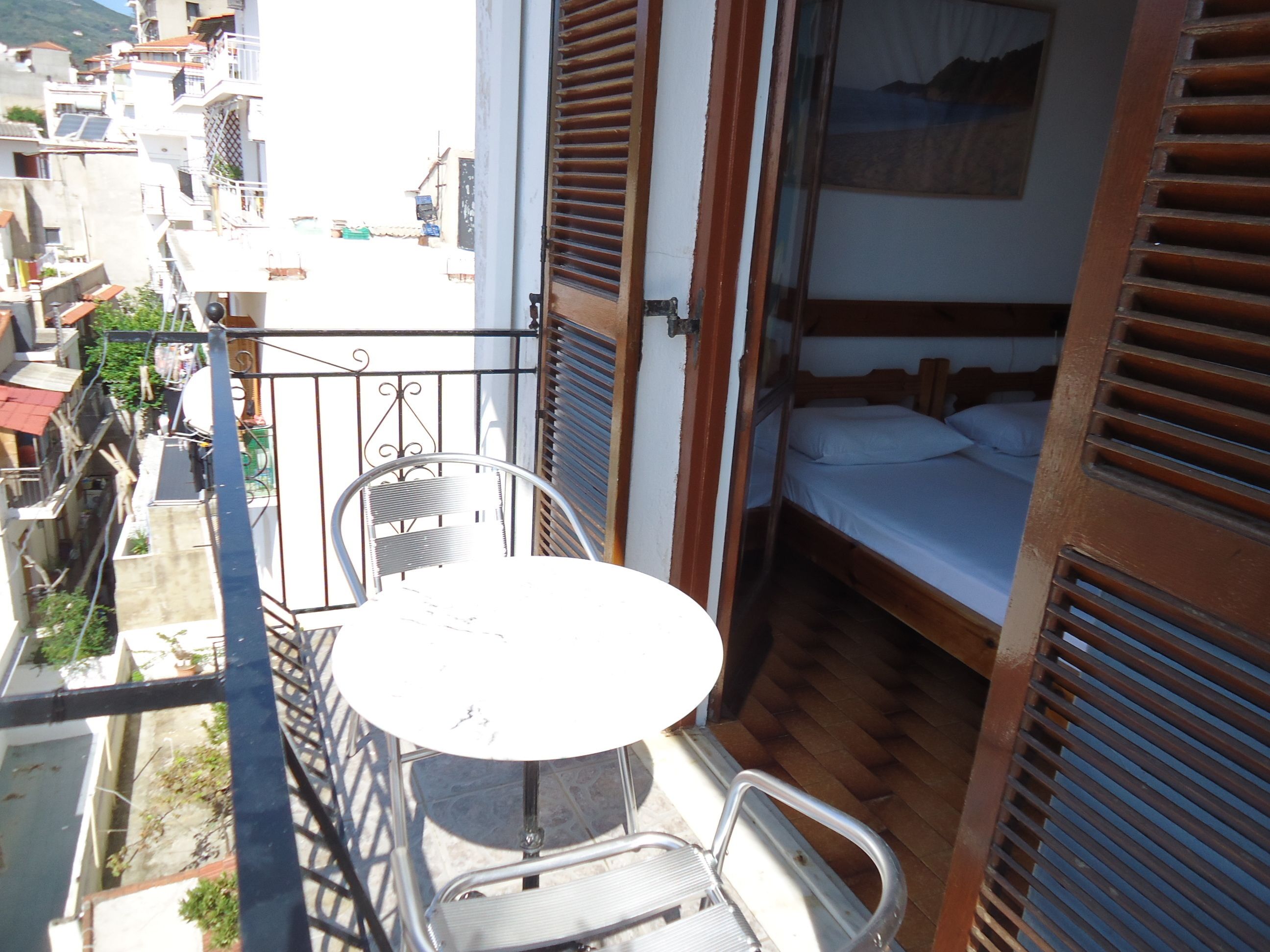 A balcony with a table and chairs, a bed, and a view of neighboring buildings.