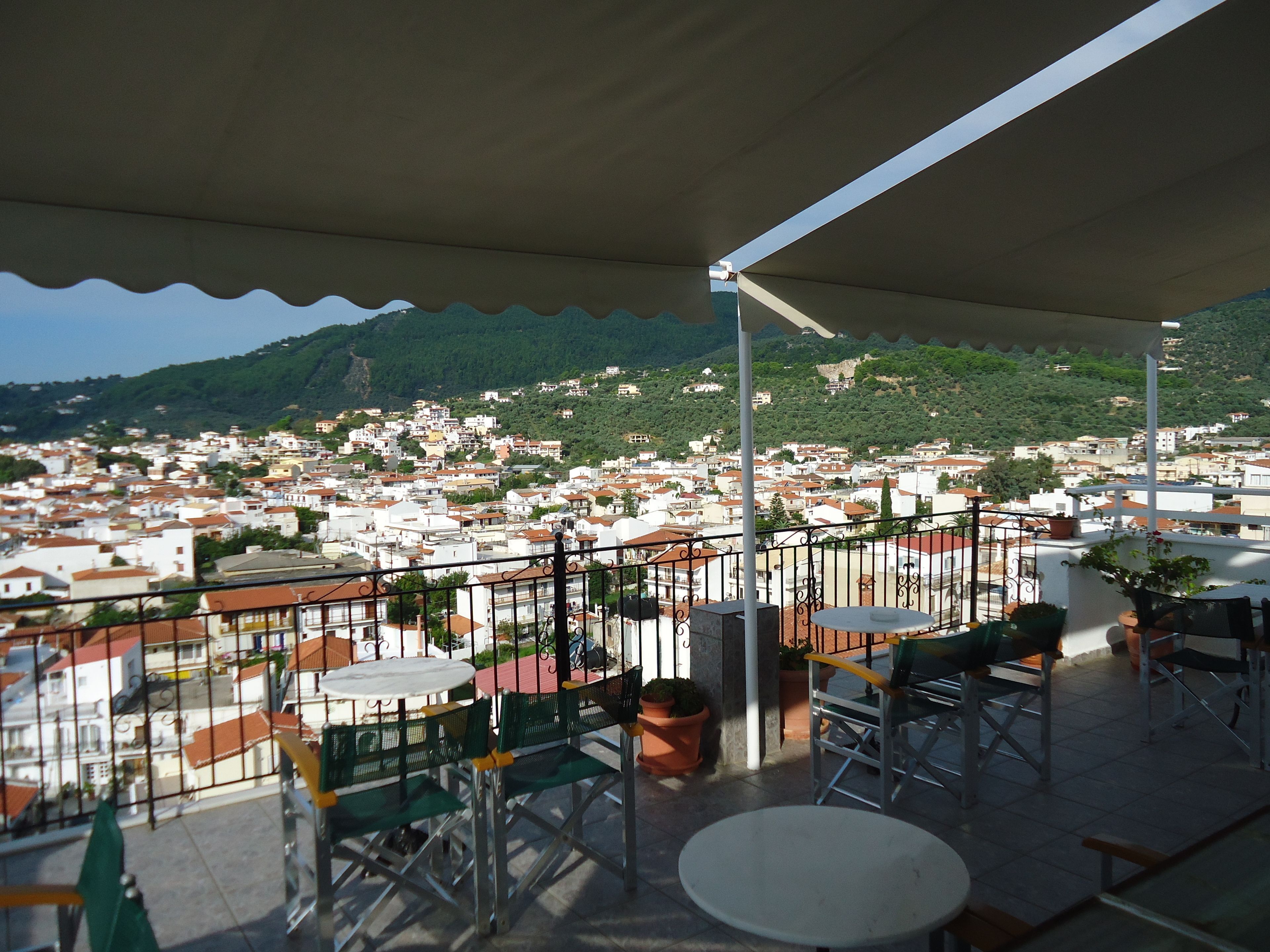 A terrace with outdoor seating, overlooking a densely packed town with buildings and a hill in the background.