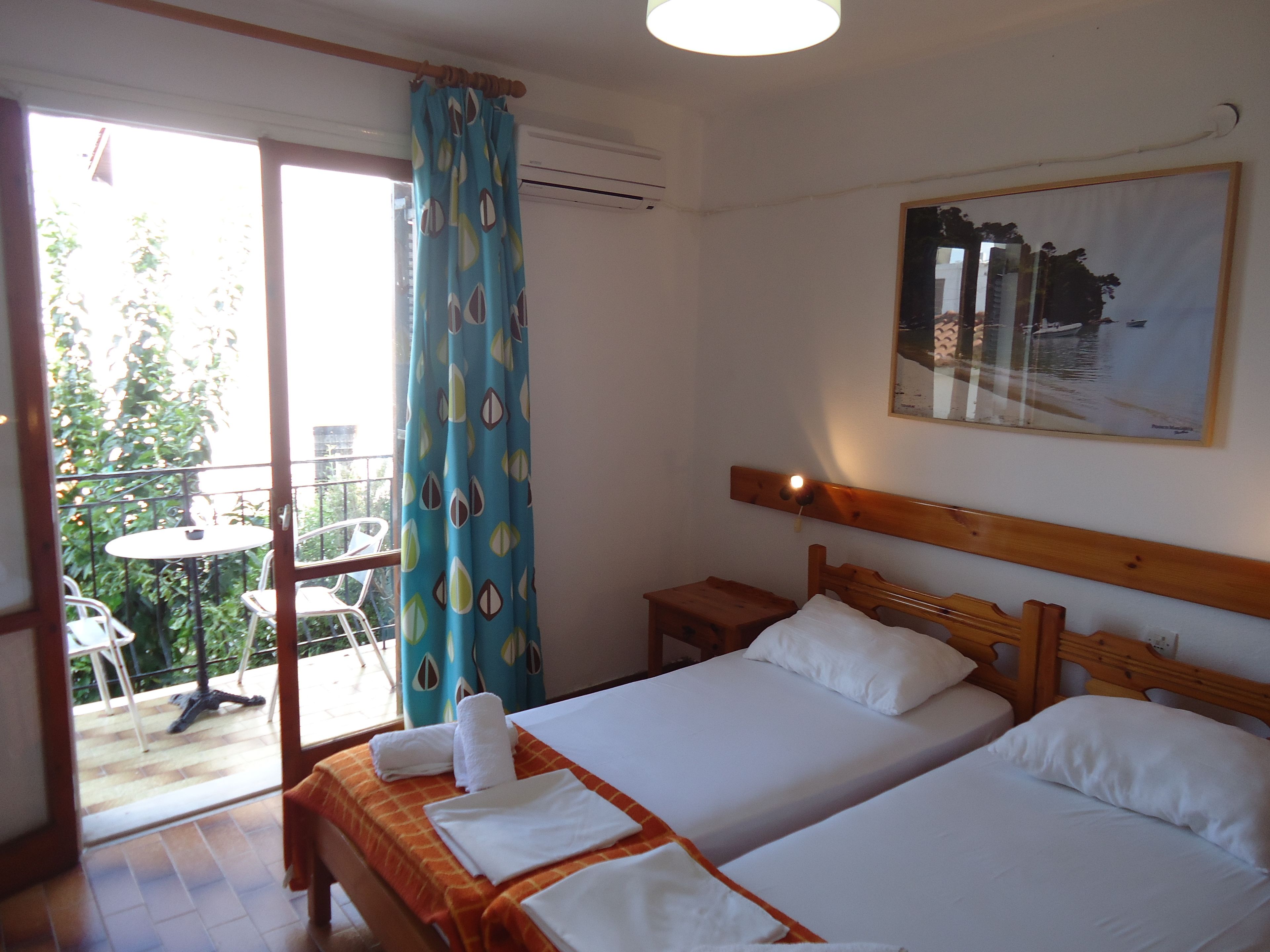 A hotel room with two beds, a balcony with a table and chairs, and a painting on the wall.