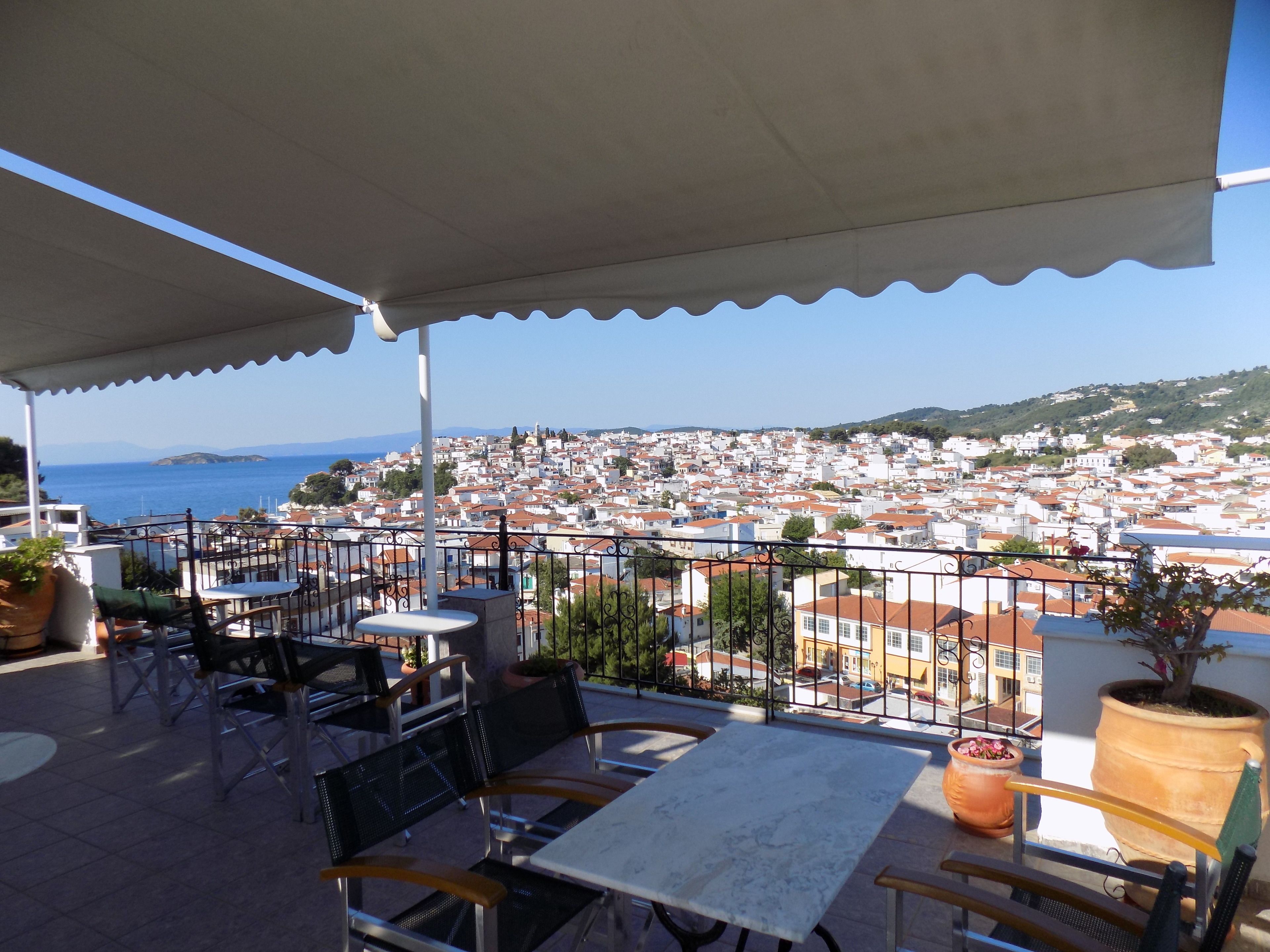Una terraza con asientos al aire libre, vistas a un pueblo costero y una planta grande en maceta.