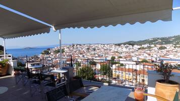 Una terraza con asientos al aire libre, vistas a un pueblo costero y una planta grande en maceta.