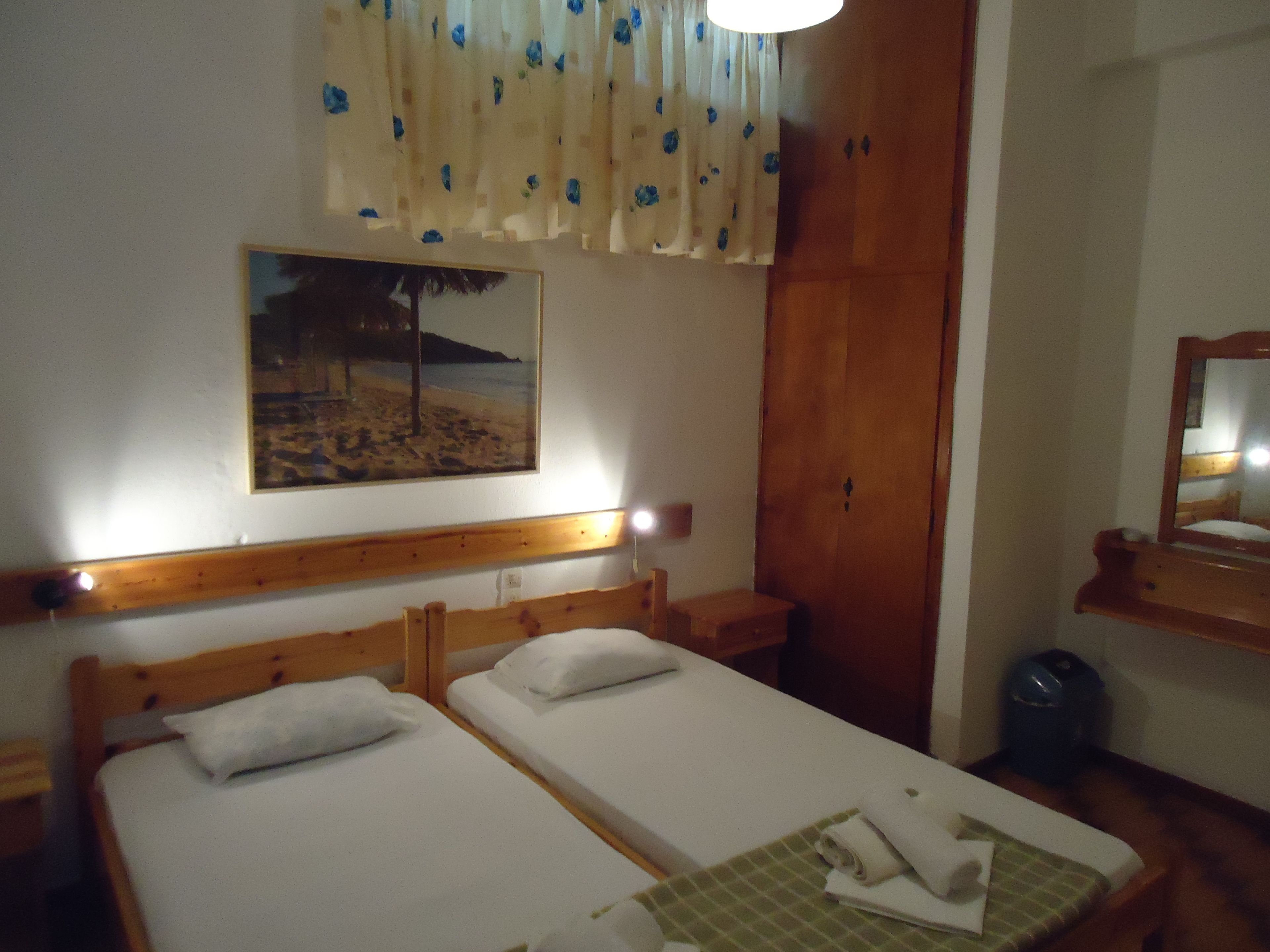 A hotel room with two single beds, a wooden headboard, a painting of a beach scene, a wooden wardrobe, and a mirror.