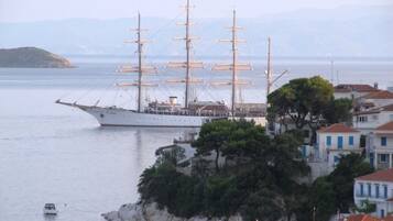 Un barco velero grande atracado cerca de un pueblo costero con edificios y una pequeña isla con árboles.