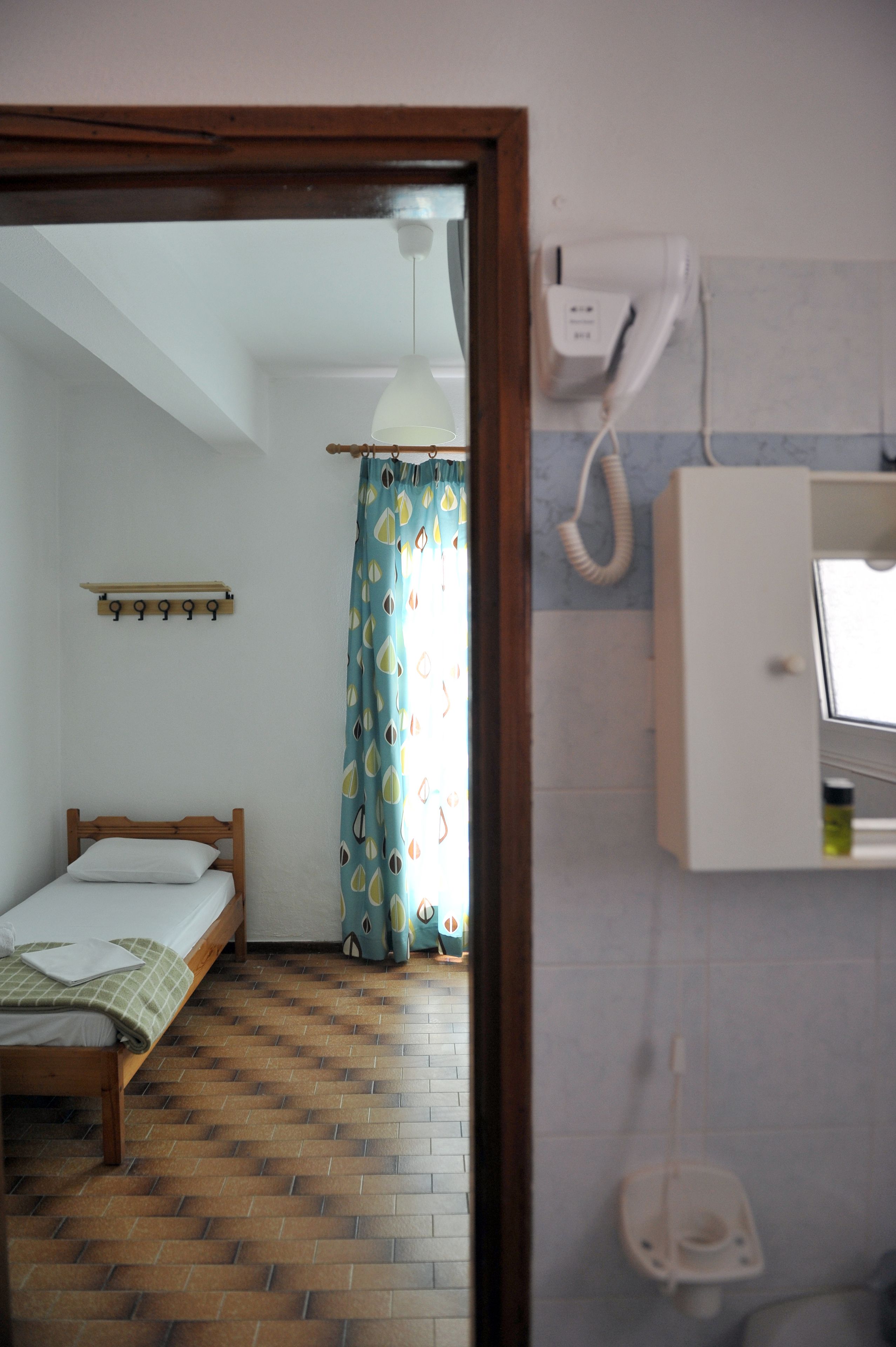 A room with a bed, a wooden headboard, a hanging light fixture, a telephone, and a bathroom with a toilet.