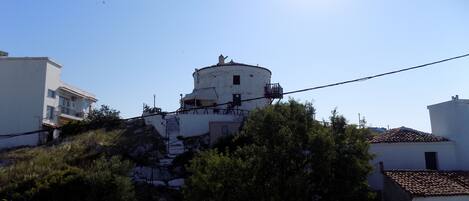 Un edificio blanco con una torre redonda sobre una colina, rodeado de vegetación y otros edificios blancos.