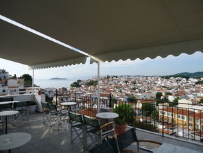 Una terraza con asientos al aire libre, vista a un pueblo costero y cielo despejado.