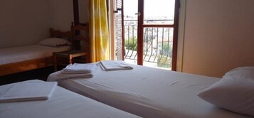 Una habitación con dos camas, una silla de madera y una ventana con vista al exterior.