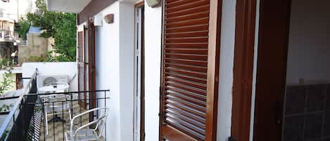 Un balcón con mesa y sillas, un tendedero y una puerta con contraventanas.