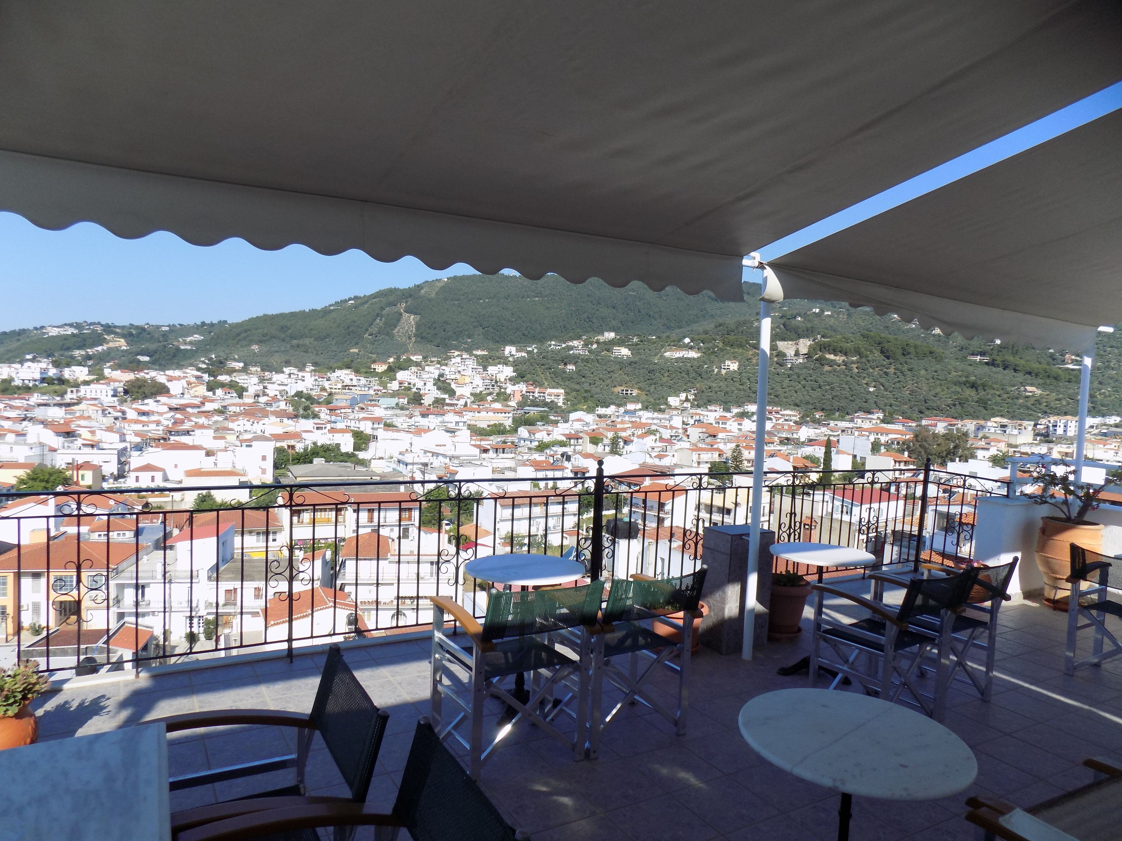 Un balcón con mobiliario exterior, con vistas a un pueblo de edificios con tejados rojos y una colina al fondo.