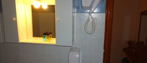 Un baño con espejo, secador de pelo y secamanos en la pared.