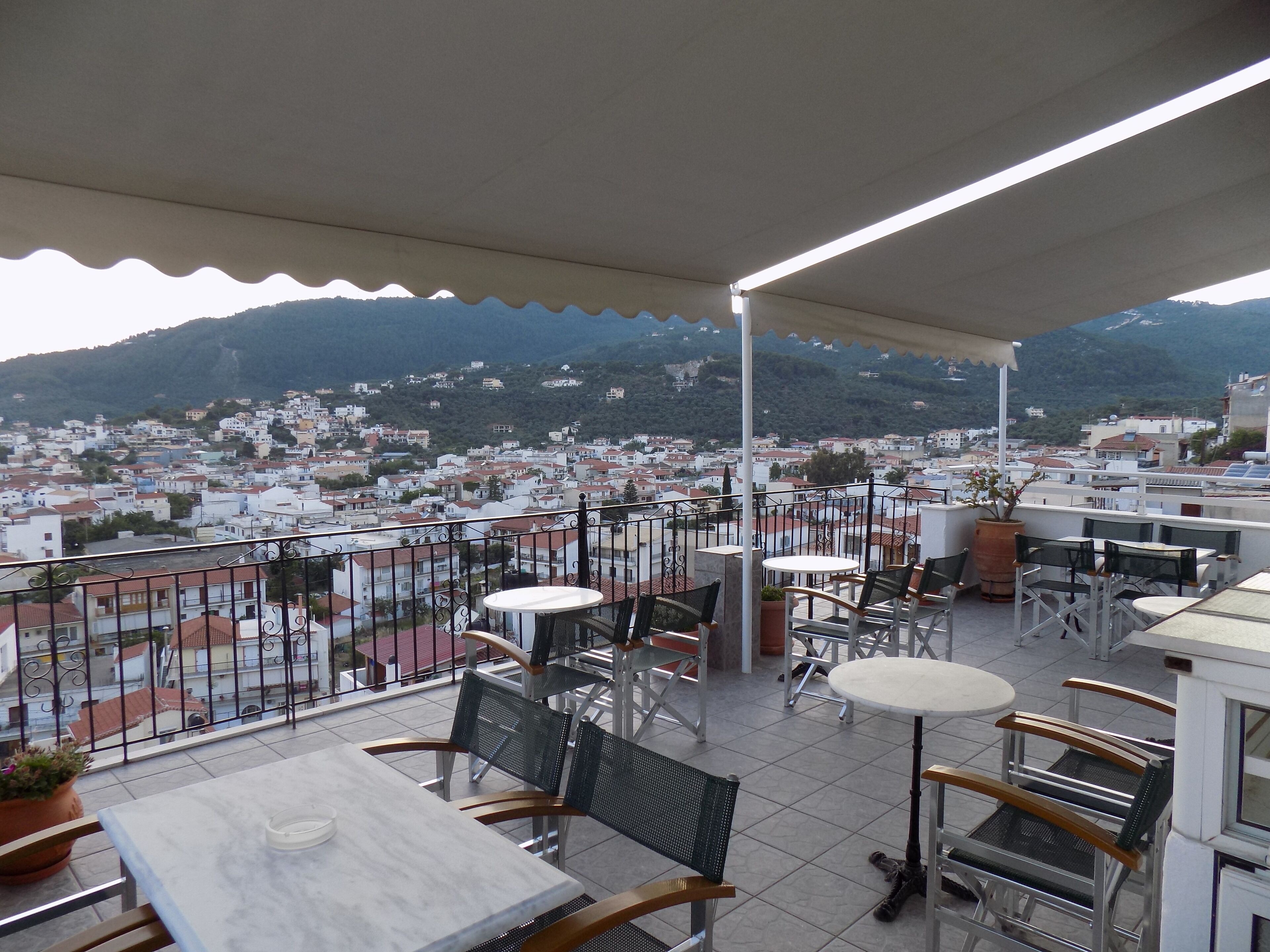 A terrace with outdoor seating, a view of a town, and mountains in the background.