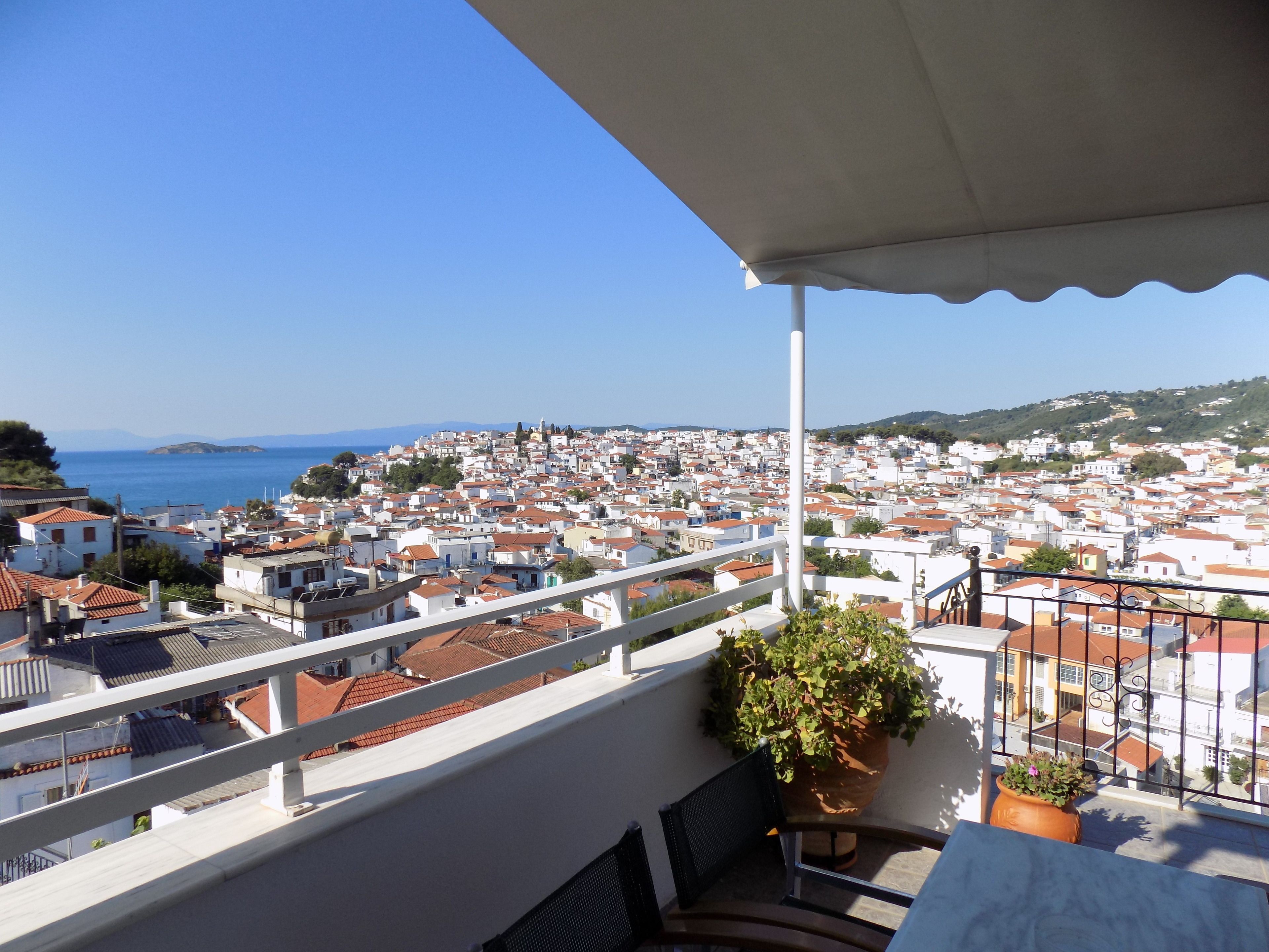 A balcony with a view of a coastal town, white buildings, and a clear blue sky.
