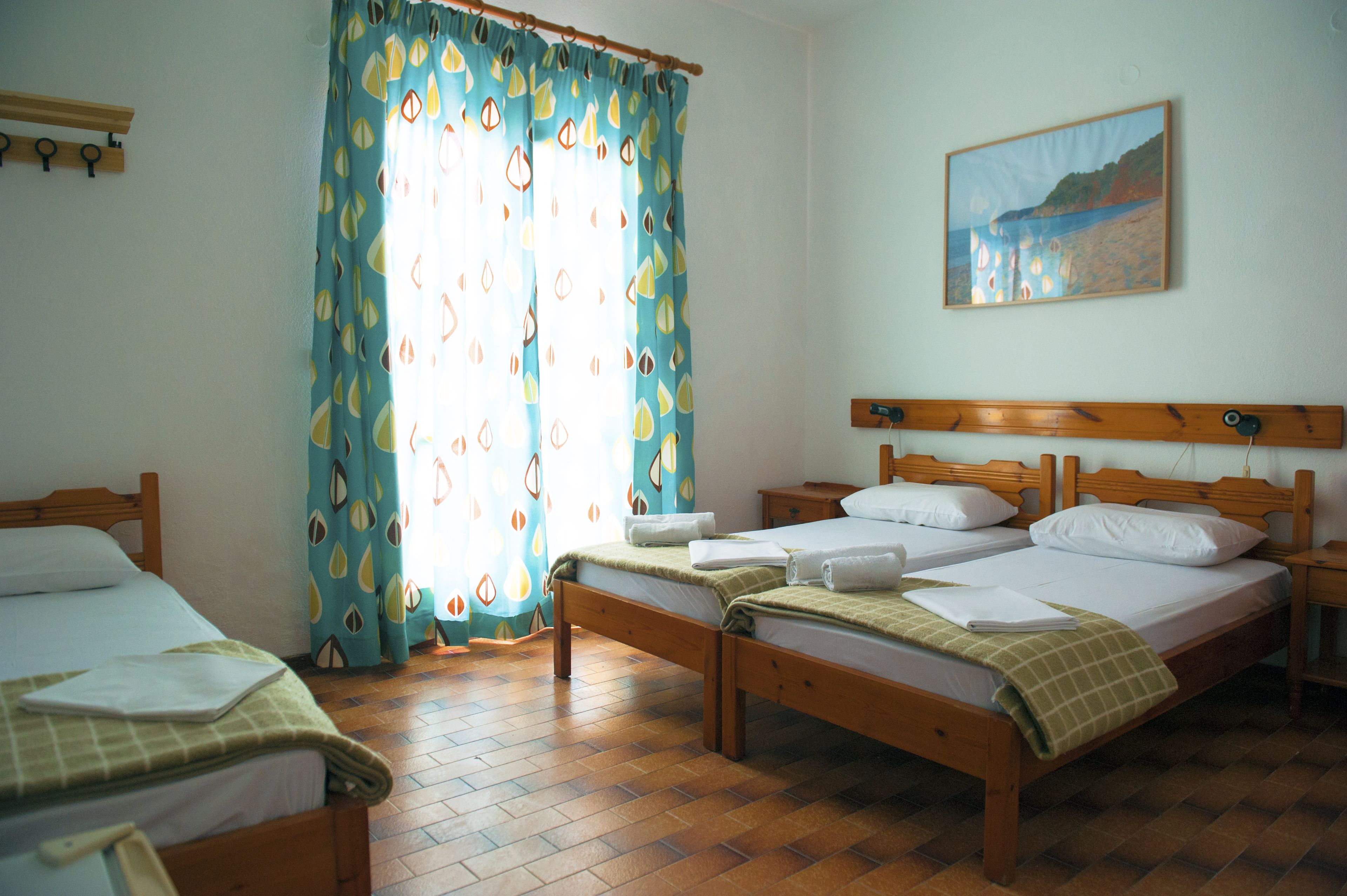 Una habitación con dos camas de madera, cabeceros de madera, un cuadro en la pared y una ventana con cortinas estampadas.