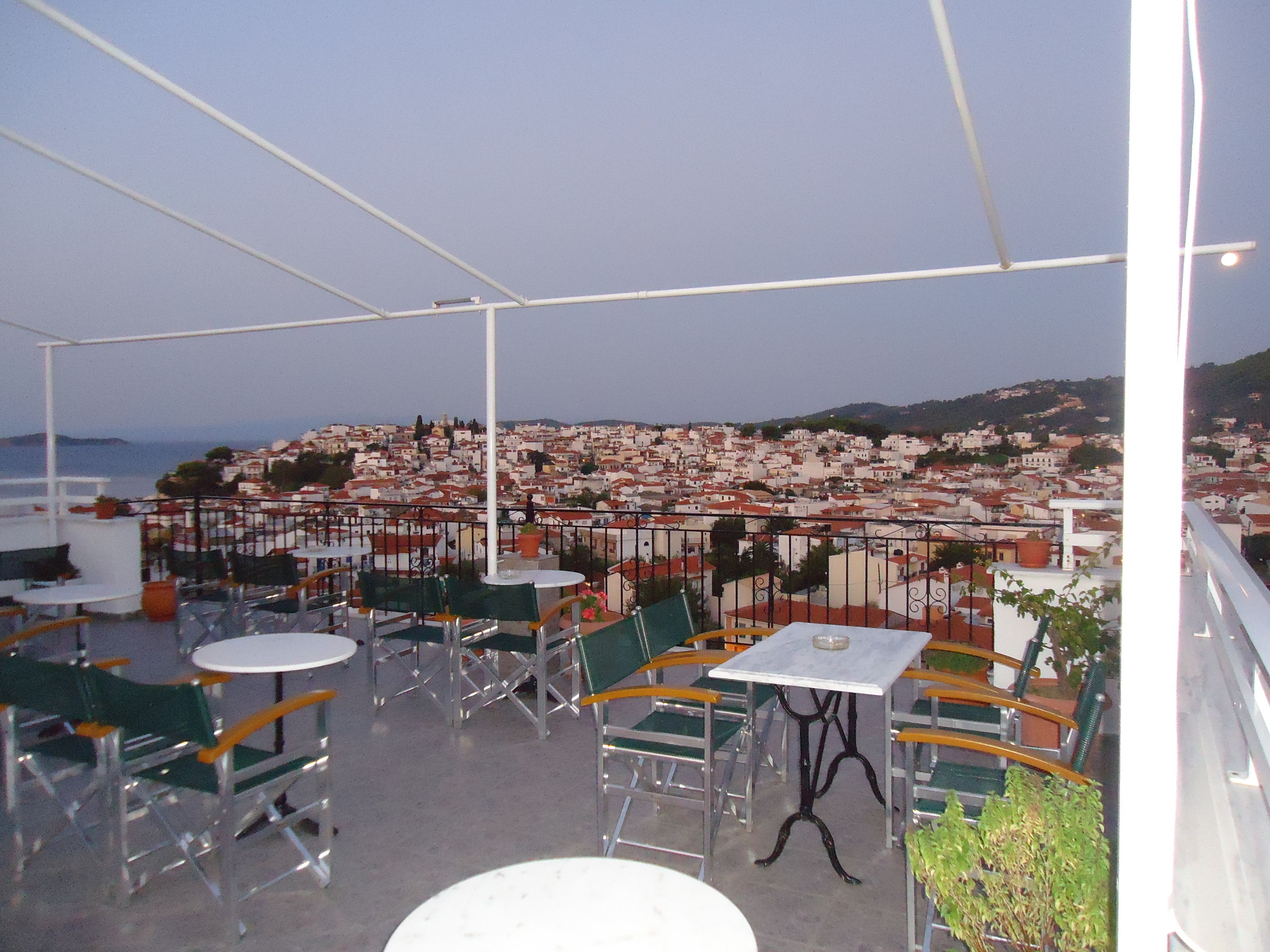 An outdoor terrace with tables and chairs, overlooking a coastal town.